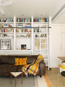 Cozy modern living space with a couch, chair, dining table, and bookshelf, decorated with books and featuring a modern and comfortable style