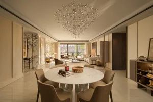 A modern dining room with a large dining table, chandelier, chairs, couch, and potted plant, creating a cozy and sophisticated atmosphere