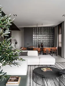A modern living room with a white couch, chair, and dining table, decorated with a vase, potted plant, and book, in a well-lit space with natural light and a clean, well-maintained atmosphere