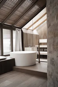 Bathroom with a white bathtub and shower, stone walls, and a wooden floor, in a dimly lit space creating a cozy atmosphere