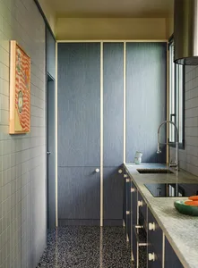 A modern kitchen with wooden cabinets, a tile floor, and a bowl of oranges on the counter, lit by natural light