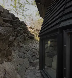 A traditional stone-built house with a black door and a window, set against a natural stone wall