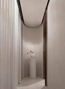 A clean and minimalist bathroom with a white vase on a pedestal, toilet visible in the background