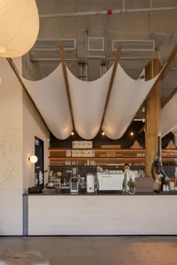 A modern coffee shop with a cozy atmosphere, featuring a counter, dining table, and white curtains, set against a warm and inviting background