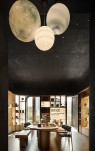 A modern living-dining space with a black ceiling, white walls, and a large window, featuring a dining table, chairs, bookshelf, and books, with soft and diffused lighting