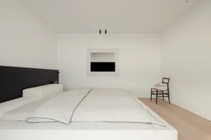 Cozy modern bedroom with a bed, chair, and fireplace, surrounded by natural light and wood accents