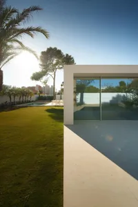 A serene white house with a glass wall surrounded by a lush green field, allowing natural light to enter and creating a bright and inviting space