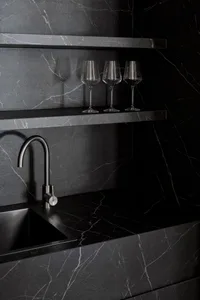 A modern kitchen with a marble counter, sink, and three wine glasses, set in a dimly lit space
