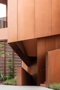 Photograph of a modern building with a brown metal facade, featuring a curved wall and a staircase leading up to the upper levels