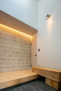 A dimly lit hallway with a wooden bench near a doorway, featuring a minimalist style with a focus on functionality and simplicity