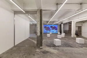 A modern lobby with a concrete floor, white storage cubes, and a large screen displaying a video, lit by dim lighting