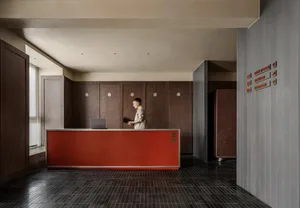A busy lobby with a red counter, a desk, and a laptop, featuring a woman and several other people in a lively atmosphere