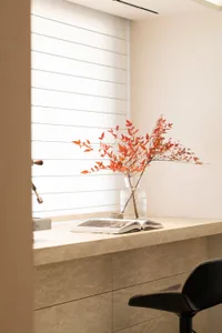 A home office with a desk, chair, and vase of flowers, featuring a mix of natural and artificial lighting