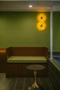 A small, cozy room with green walls, a wooden bench, and a green cushion, lit by a wall light