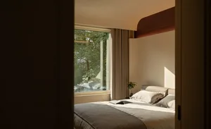 A well-lit bedroom with a bed, window, and curtain, featuring a white comforter and two pillows
