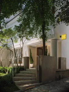 Photograph of a modern building with a white facade, featuring a concrete staircase and a wooden door, under natural light