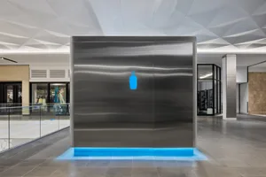 A modern building with a silver wall featuring a blue bottle design, visible interior, and clean lines, set against a bright and inviting background