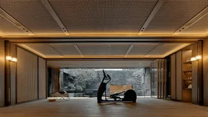 A dimly lit living space with a modern style, featuring a large sculpture on a bench, a dining table, and chairs, with a combination of wood and metal elements