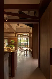 Cozy modern restaurant interior with a wooden dining table and chairs, dim lighting, and a visible kitchen counter in the background