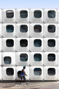 A photograph of a building with a unique design featuring a large number of windows arranged in a square pattern, set against an urban backdrop