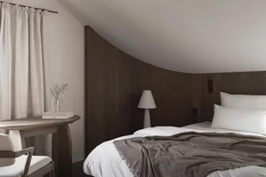 Cozy bedroom with a wooden bed frame, a wooden floor, and a dimly lit atmosphere, featuring a bed, a table, and a lamp