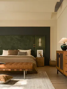 A well-lit bedroom with a bed, bench, and dresser, featuring a green headboard and neutral colors