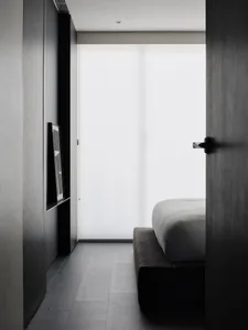 Dimly lit bedroom with a bed, TV, and window, creating a cozy atmosphere with natural light