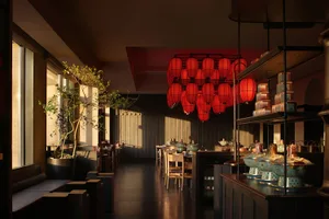 Modern restaurant with a black and white color scheme, wooden furniture, and red lanterns, featuring a dining area and bar in a dimly lit space