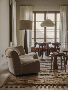 Cozy living room with a couch, chair, and dining table, featuring a rug, wood, and fabric, with soft and diffused lighting