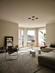 A well-lit living room with a couch, chair, and glass table, furnished with a potted plant, vase, and book, creating a modern and inviting space for relaxation and socializing