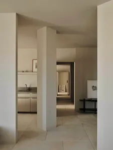 A bright and airy kitchen and hallway area with a sink, refrigerator, dining table, and natural light from windows