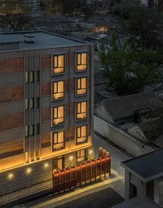 A dimly lit hotel lobby with a brick exterior, large windows, and a balcony, featuring a bench and dining table