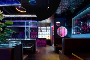 A modern restaurant with a bar area, black and purple colors, and dim lighting creating a sophisticated and inviting atmosphere