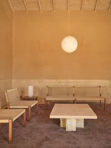 A warm and inviting room with a wooden floor, stone wall, and wooden furniture, including a table and chairs, encouraging social interaction and relaxation