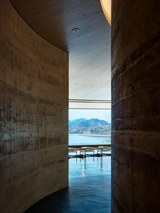 A modern restaurant with a large dining table and chairs, surrounded by a large window offering a view of the water outside, with natural light and a comfortable atmosphere