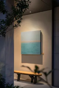 A serene impressionistic painting of a beach scene with a boat in the distance, displayed on a wall with a calming atmosphere