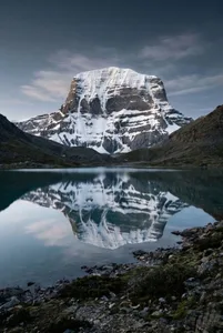A serene mountain landscape with a snow-covered peak reflected in a calm lake, surrounded by natural beauty