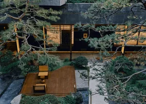 A serene outdoor space with a wooden deck surrounded by trees, a stone patio, and a stone building exterior
