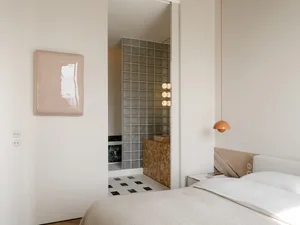 A bedroom with a bed, chair, and lamp, featuring a white color scheme and cozy atmosphere