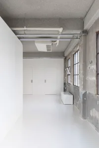 A large, open room with a white floor and white walls, natural light from a window, and a door, creating a calm and serene atmosphere