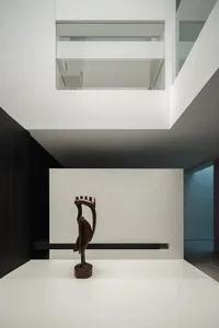 一隻鳥像似的雕像坐在一張白色桌子上，在一個白牆和玻璃天花板的現代房間中，低調照明