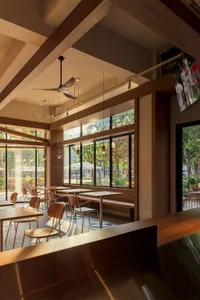 A modern restaurant interior with a dining area and bar, featuring wooden elements, soft warm lighting, and a contemporary color scheme