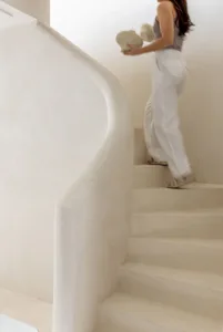 A woman walks up a white marble staircase in a bright and airy space with natural light