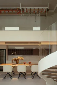 A modern kitchen with a dining table and chairs, surrounded by a refrigerator, oven, and sink, with natural light and a vase with flowers