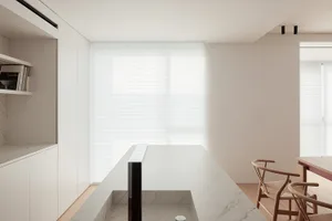 A modern kitchen with a white marble countertop, a built-in sink, a refrigerator on the left, an oven on the right, and a chair nearby, under bright lighting