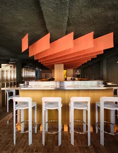 A modern restaurant interior with a bar, stools, and vibrant orange and red decorations in a well-lit space