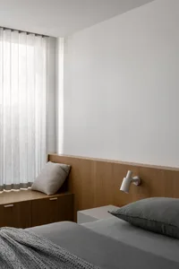 Cozy bedroom with a wooden bench, white walls, and a window with curtains, lit by a lamp