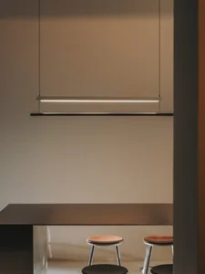 A modern kitchen with a wooden table and chairs, metal lighting, and a refrigerator in the background, set against a white wall and black countertop