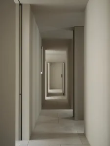 A dimly lit, narrow hallway with a concrete floor and walls, featuring a doorway at the end