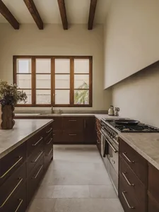 A modern kitchen with a white color scheme, marble countertops, and a large window allowing natural light to enter, creating a bright and welcoming atmosphere
